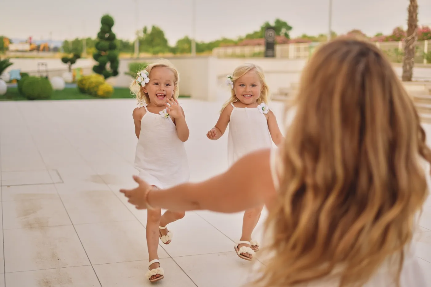 Two little girls in white dresses running to their mum, laughing, during a family photoshoot